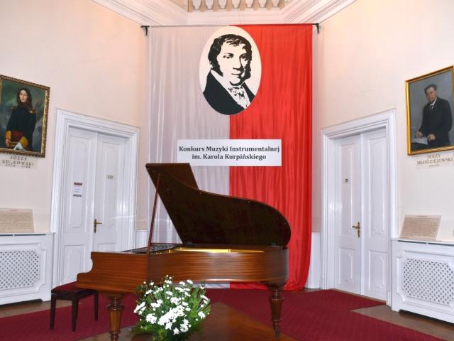 Fortepian w Sali Trójkątnej Pałacu Sułkowskich we Włoszakowicach, w tle biało-czerwona flaga z podobizną Karola Kurpińskiego i nazwą konkursu