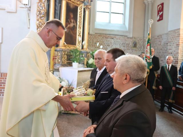 Ksiądz proboszcz Zbigniew Dobroń odbiera od delegacji słoiki z miodem