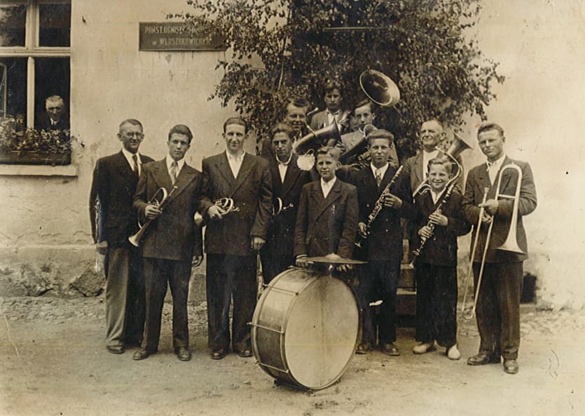 Ludwik Benyskiewicz (pierwszy z lewej) z orkiestrą dętą ówczesnego Państwowego Ogniska Muzycznego we Włoszakowicach przed budynkiem Ogniska (lata 60. XX w.)